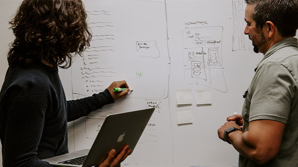 Two men take notes on a whiteboard 